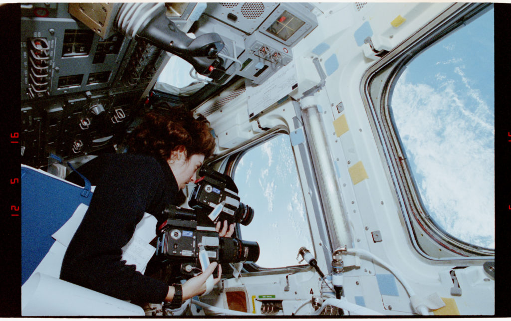 Ochoa in a space shuttle looking out a window down to Earth