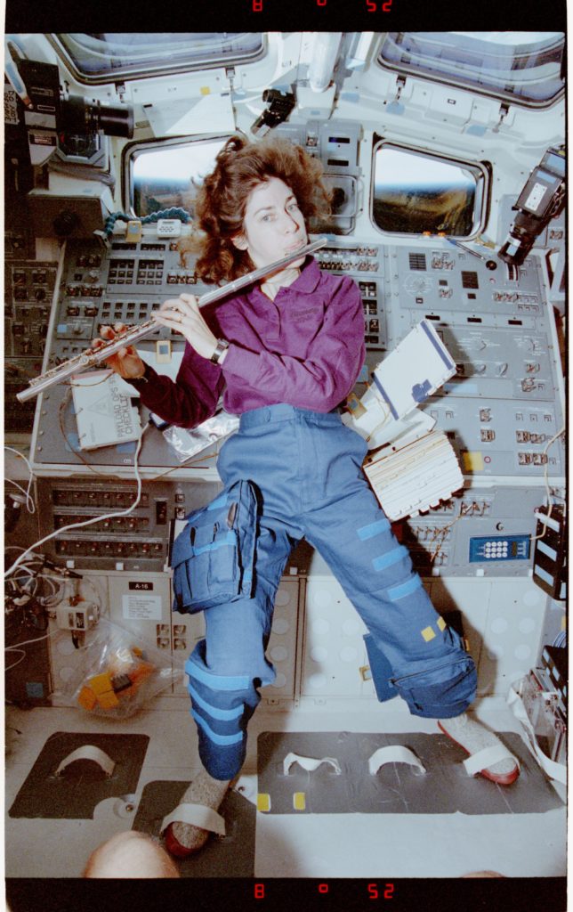 Ochoa playing flute. Feet are strapped down to hold her in place in 0 gravity