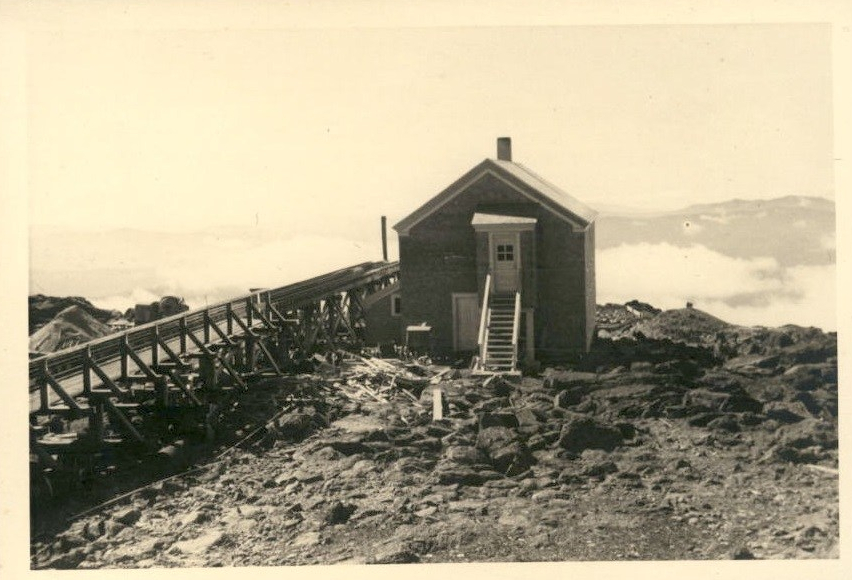 Image of a small building on top of a mountain with clouds in the background.