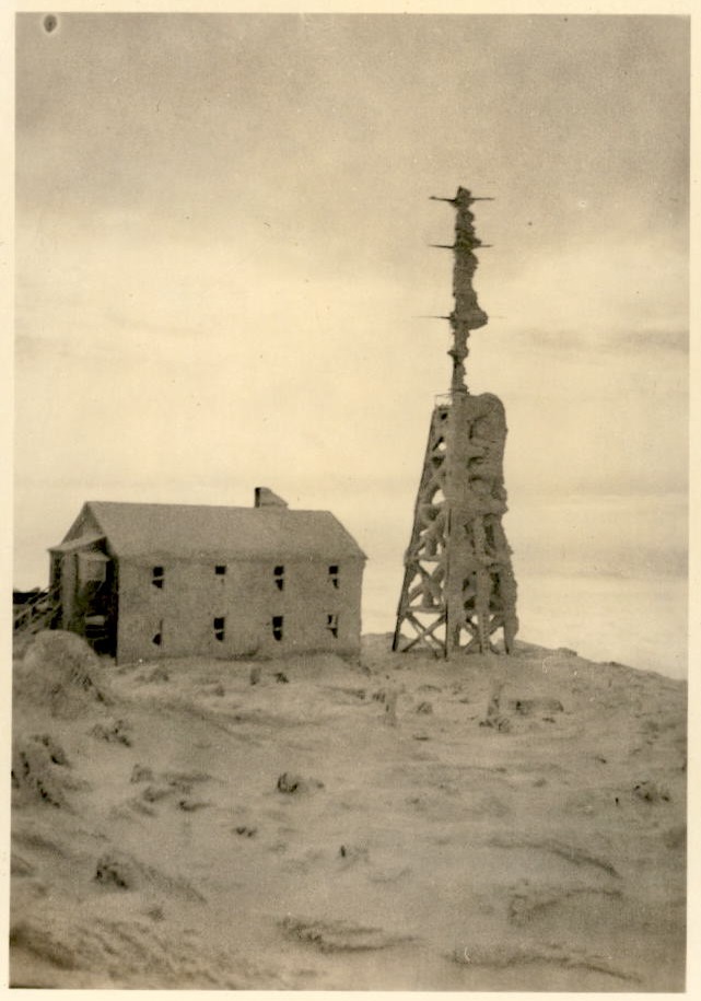 Image of radio tower and building adjacent to it covered with snow.