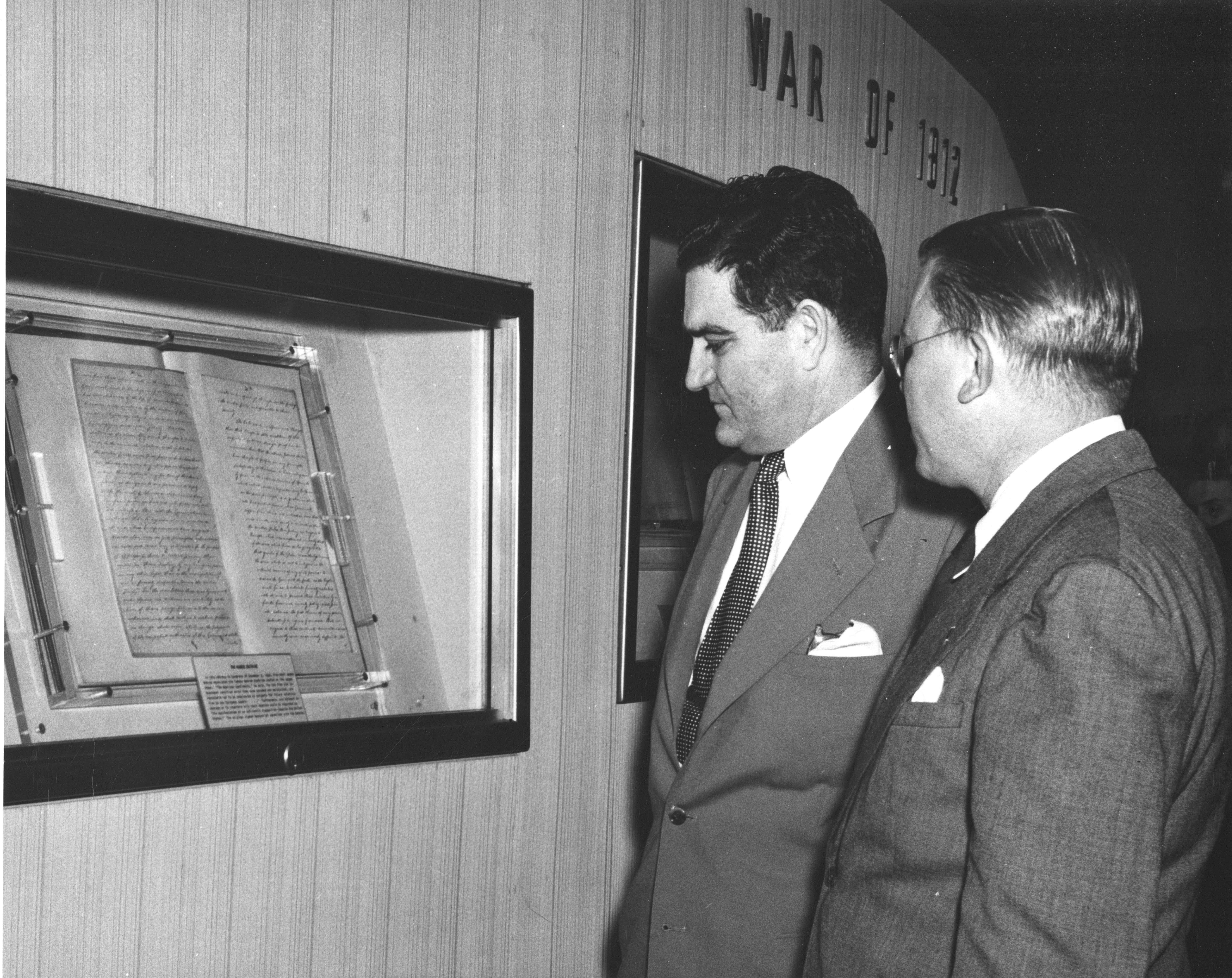 two men viewing document inside glass case.